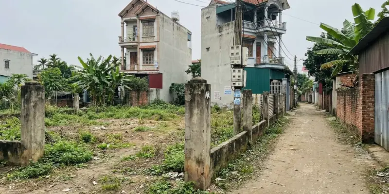 Thửa đất trống có mốc ranh giới bê tông nằm cạnh dãy nhà phố đã xây ở vùng ven đô thị Việt Nam