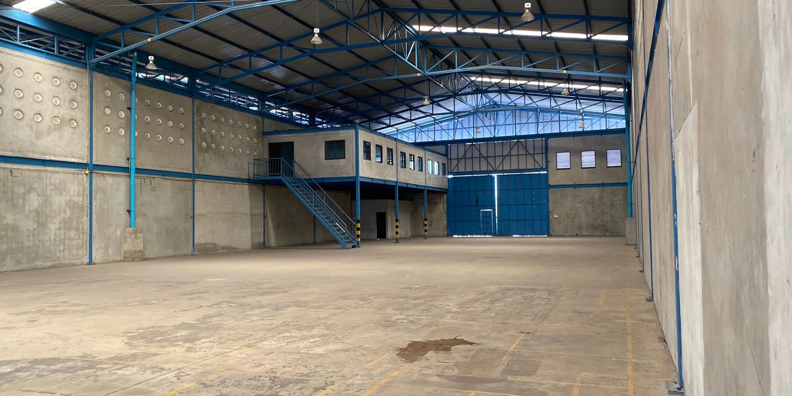 Ảnh bên trong một nhà xưởng trống khung thép xanh, tường gạch và sàn bê tông, minh họa công trình sản xuất xây trên đất cơ sở sản xuất phi nông nghiệp