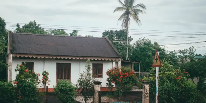 Ngôi nhà mái tôn tường trắng có vườn hoa phía trước ở Buôn Ma Thuột, minh họa mảnh đất gia đình được cho bằng giấy tay
