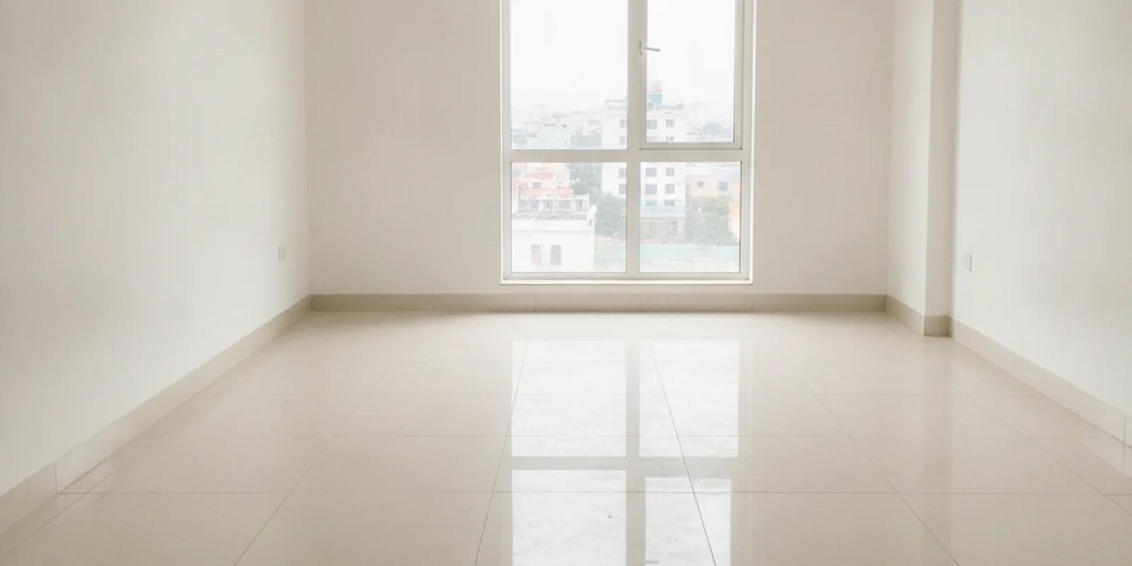 Ảnh căn hộ chung cư trống vừa bàn giao, sàn gạch sáng màu, tường trắng và cửa sổ lớn, minh họa việc đo lại diện tích thông thủy khi nhận nhà