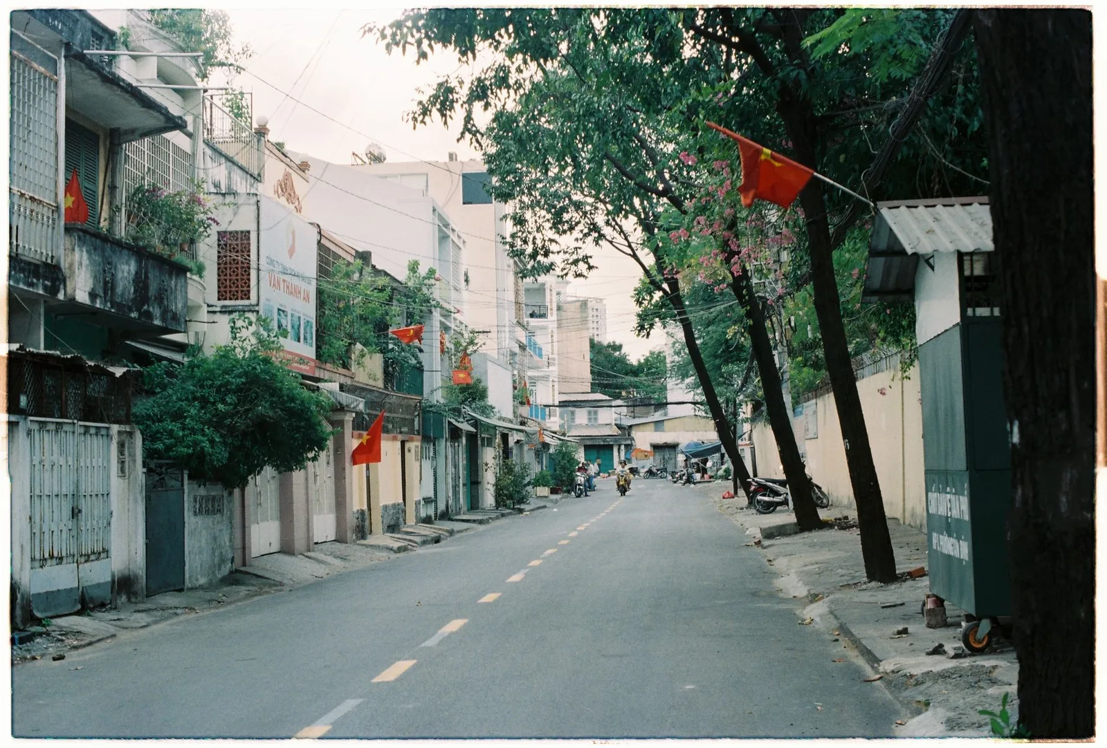 Con phố yên tĩnh ở Việt Nam với dãy nhà mặt tiền hai bên đường và hàng cây, minh họa nhà mặt đường có phần đất có thể dính lộ giới